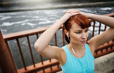 Buy stock photo Shot of a sporty young woman listening to music while out for a run in the city