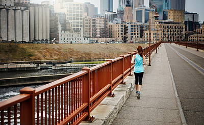 Buy stock photo Rear view shot of a sporty young woman running in the city