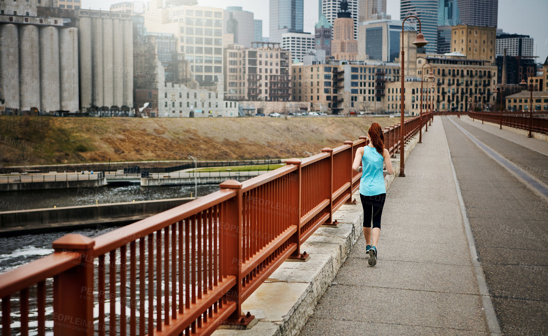 Buy stock photo Rear view shot of a sporty young woman running in the city