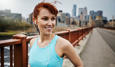 Buy stock photo Shot of a sporty young woman listening to music while out for a run in the city