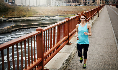 Buy stock photo Shot of a sporty young woman listening to music while running in the city