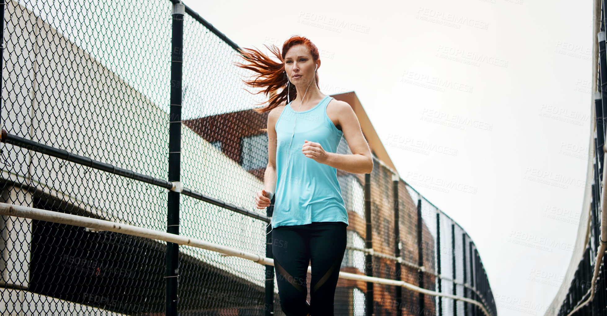 Buy stock photo Shot of a sporty young woman listening to music while running in the city