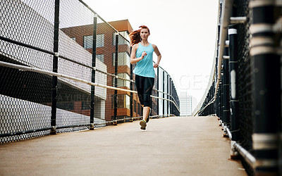 Buy stock photo Shot of a sporty young woman listening to music while running in the city