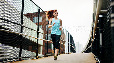 Buy stock photo Shot of a sporty young woman listening to music while running in the city