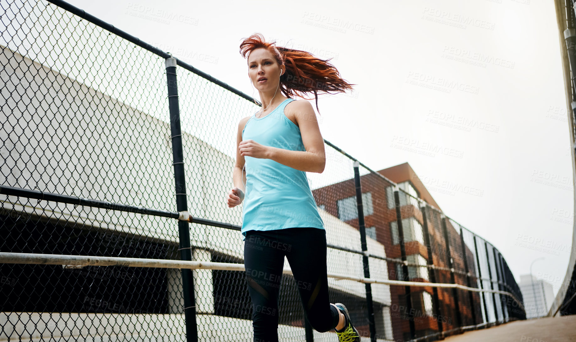 Buy stock photo Shot of a sporty young woman listening to music while running in the city