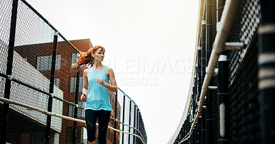 Buy stock photo Shot of a sporty young woman listening to music while running in the city