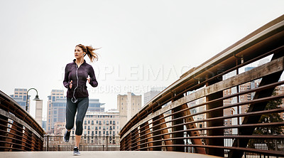 Buy stock photo Full length shot of an attractive young woman listening to music while running through the city