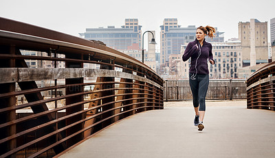 Buy stock photo Full length shot of an attractive young woman listening to music while running through the city