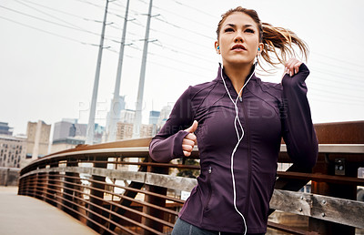 Buy stock photo Cropped shot of an attractive young woman listening to music while running through the city