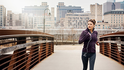 Buy stock photo Cropped shot of an attractive young woman listening to music while running through the city