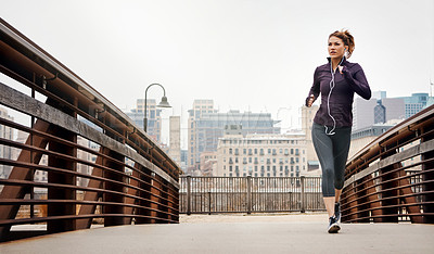 Buy stock photo Full length shot of an attractive young woman listening to music while running through the city