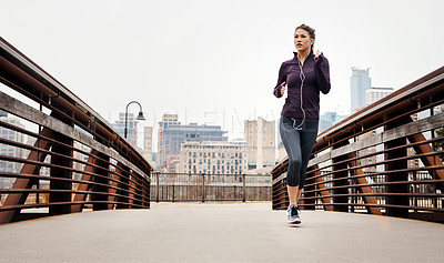 Buy stock photo Full length shot of an attractive young woman listening to music while running through the city