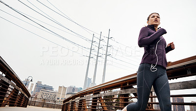 Buy stock photo Low angle shot of an attractive young woman listening to music while running through the city