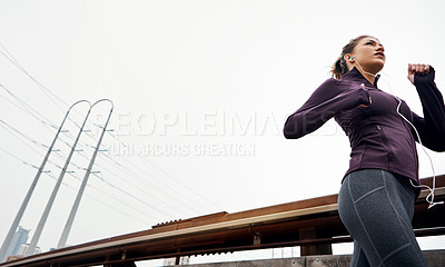 Buy stock photo Low angle shot of an attractive young woman listening to music while running through the city