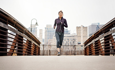 Buy stock photo Full length shot of an attractive young woman listening to music while running through the city