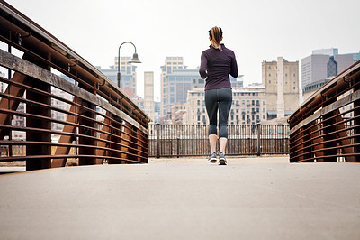 Buy stock photo Rearview shot of an unrecognizable young woman taking a run through the city