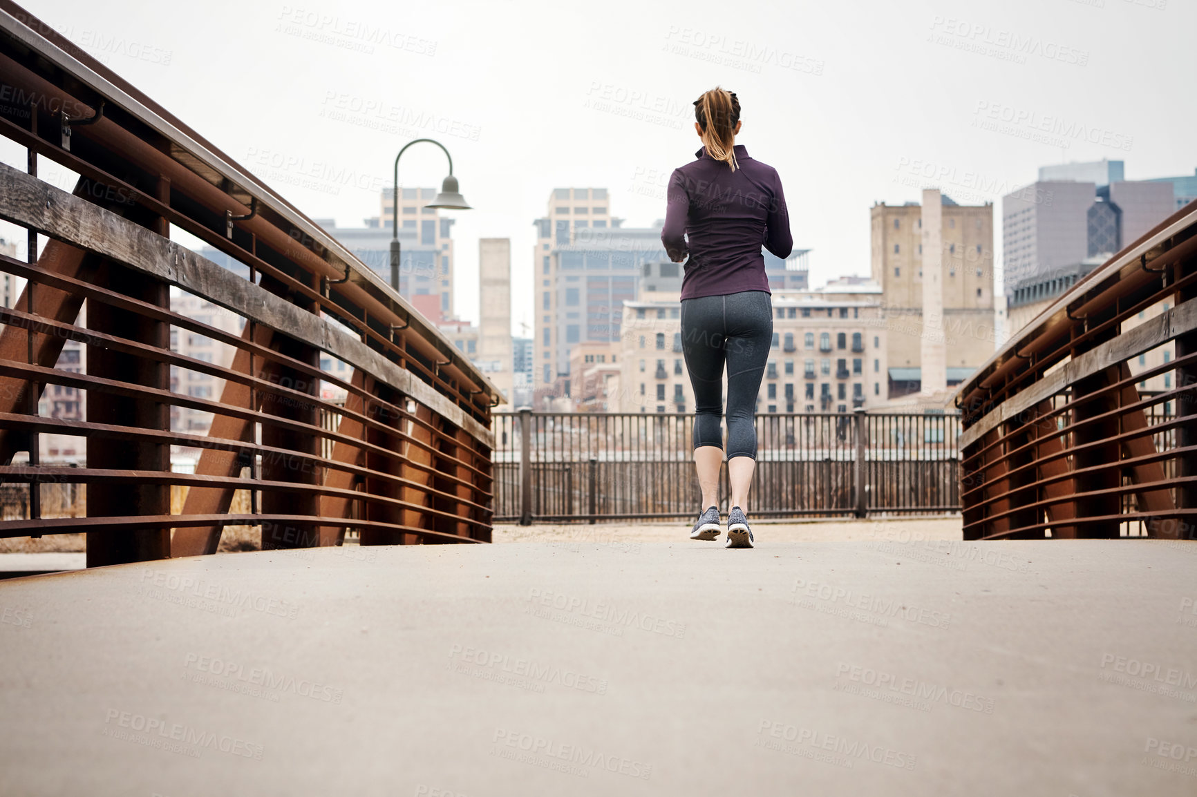 Buy stock photo Rearview shot of an unrecognizable young woman taking a run through the city