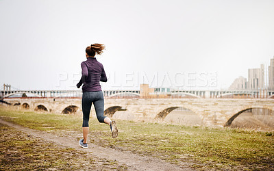 Buy stock photo Rearview shot of an unrecognizable young woman taking a run alongside the city