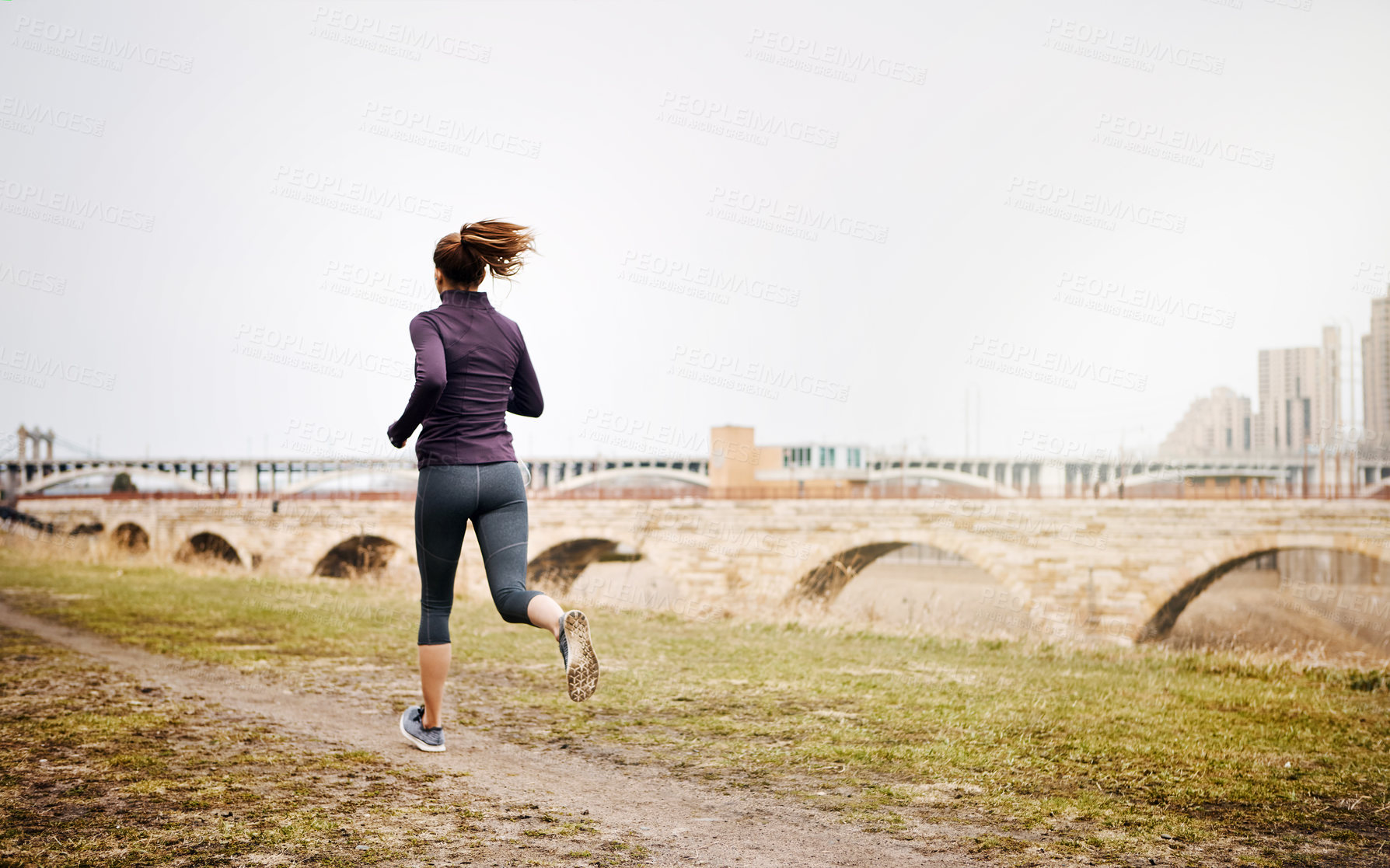 Buy stock photo Rearview shot of an unrecognizable young woman taking a run alongside the city