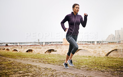 Buy stock photo Full length shot of an attractive young woman listening to music while running alongside the city