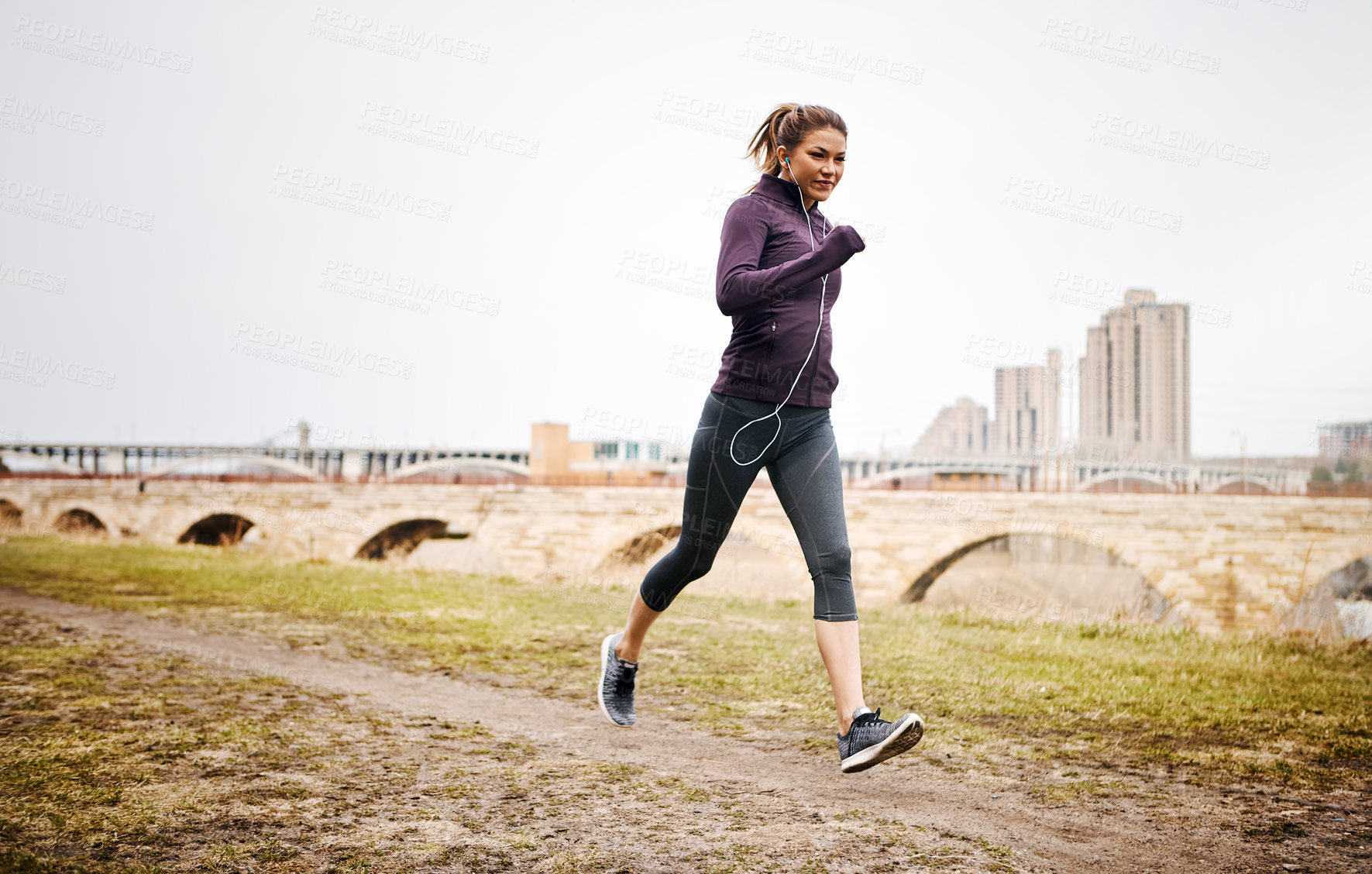 Buy stock photo Full length shot of an attractive young woman listening to music while running alongside the city