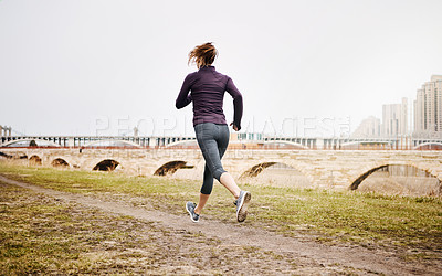 Buy stock photo Rearview shot of an unrecognizable young woman taking a run alongside the city