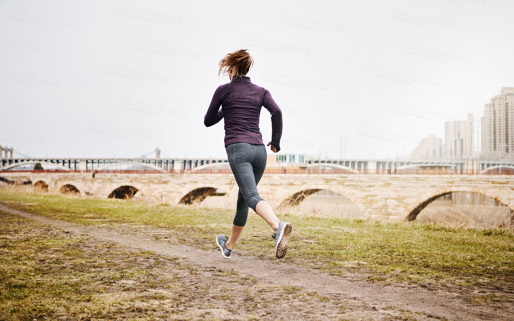 Buy stock photo Rearview shot of an unrecognizable young woman taking a run alongside the city