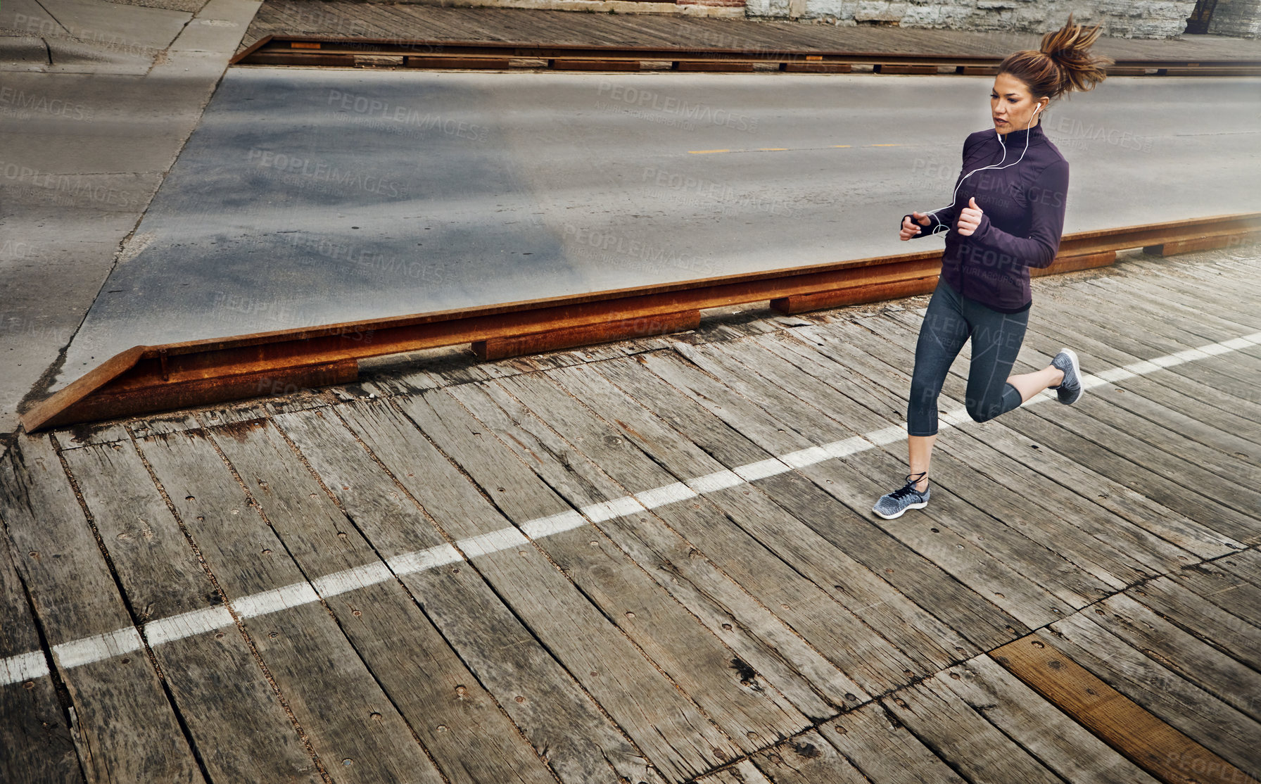 Buy stock photo Full length shot of an attractive young woman listening to music while running through the city