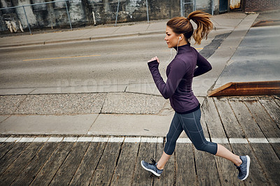 Buy stock photo Full length shot of an attractive young woman listening to music while running through the city