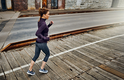 Buy stock photo Full length shot of an attractive young woman listening to music while running through the city