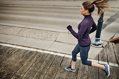 Buy stock photo Full length shot of an attractive young woman listening to music while running through the city