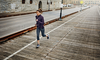 Buy stock photo Full length shot of an attractive young woman listening to music while running through the city