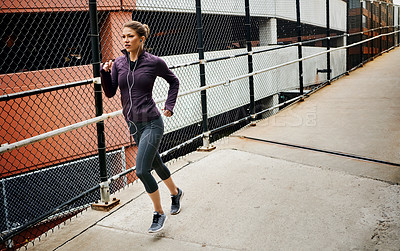 Buy stock photo Full length shot of an attractive young woman listening to music while running through the city