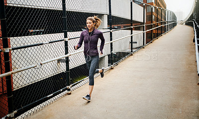 Buy stock photo Full length shot of an attractive young woman listening to music while running through the city