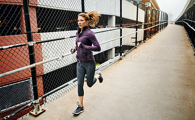 Buy stock photo Full length shot of an attractive young woman listening to music while running through the city