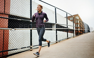 Buy stock photo Full length shot of an attractive young woman listening to music while running through the city