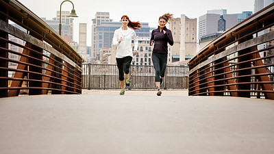 Buy stock photo Full length shot of two attractive young women running through the city