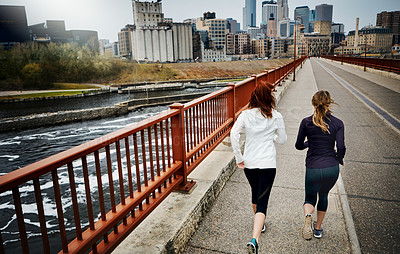 Buy stock photo Rearview shot of two unrecognizable young women running through the city