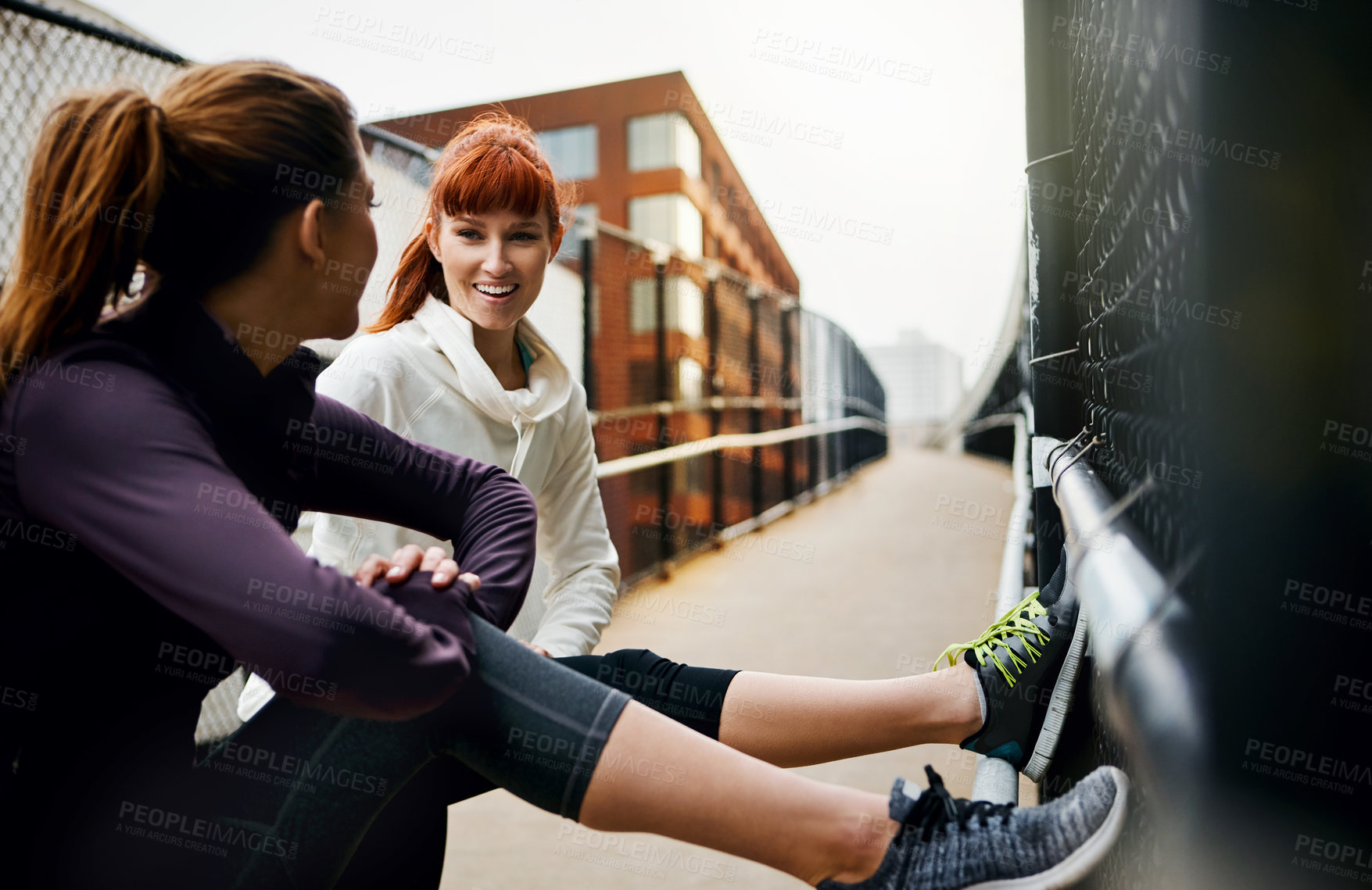 Buy stock photo Cropped shot of two attractive young women stretching before their run in the city