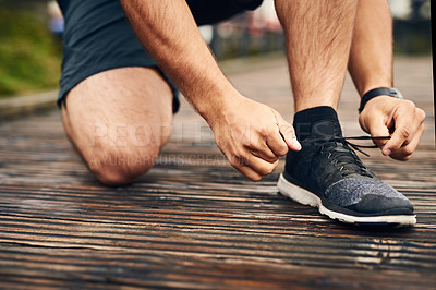Buy stock photo Closeup shot of a sporty young man tying his shoelaces while exercising outdoors