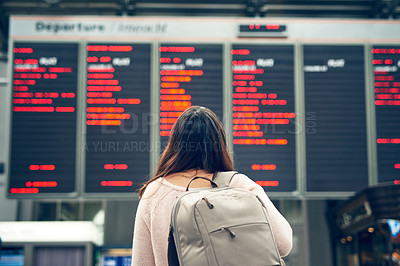 Buy stock photo Rearview shot of an unrecognizable young woman looking at an arrivals and departures board while standing in an airport