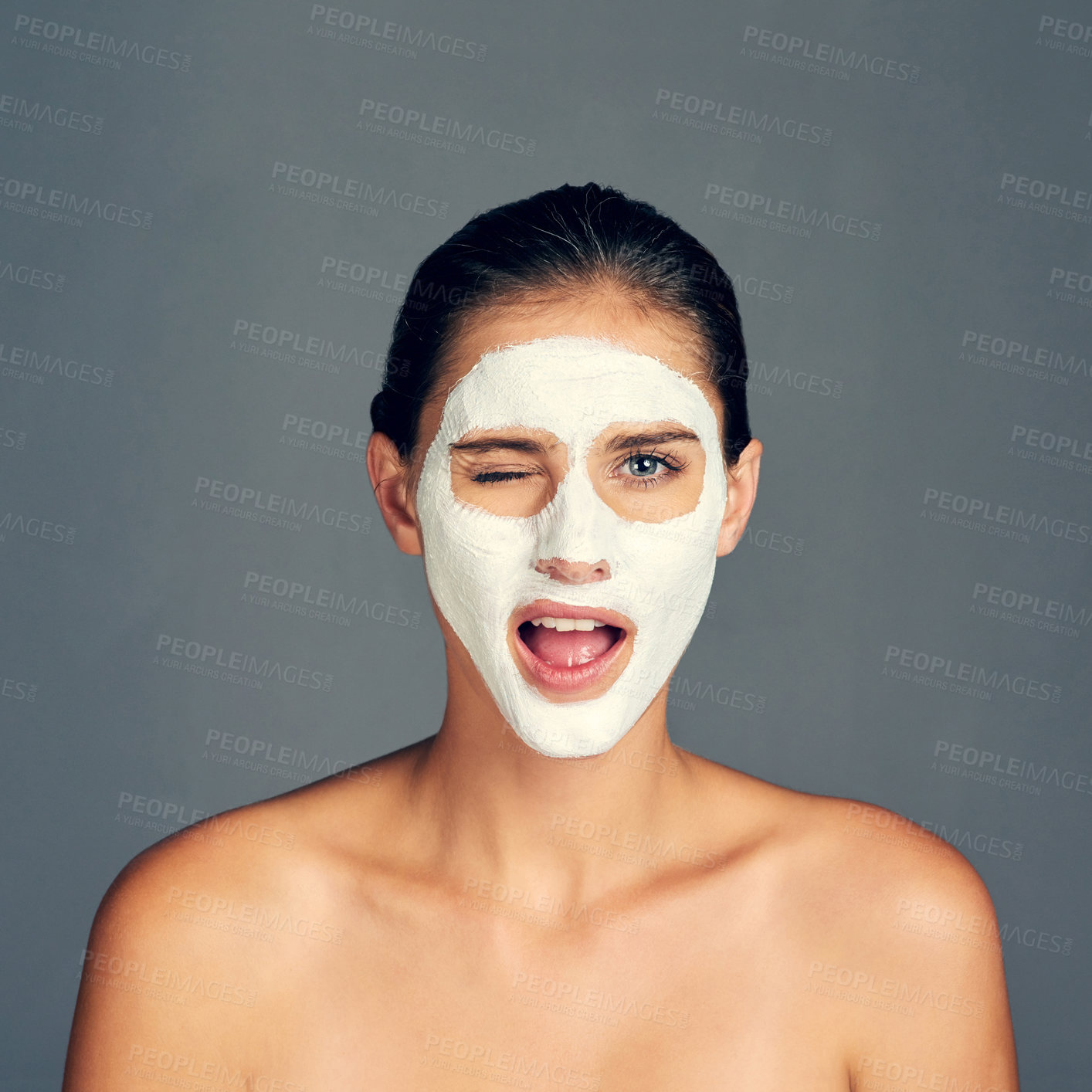 Buy stock photo Skincare, woman and wink with face mask in studio for beauty, self care and cosmetics on gray background. Female person, portrait and cream for facial, transformation and routine with detox treatment