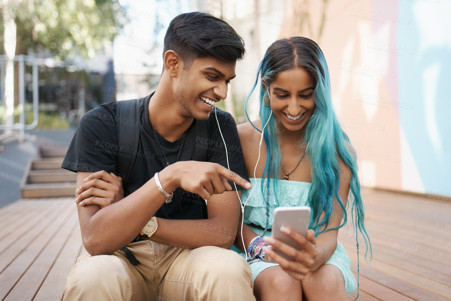 Buy stock photo Couple, earphones and laughing with mobile phone for funny meme, comic or watching video on campus. Headphones, Indian man and woman with smartphone for social media, online app or web browsing