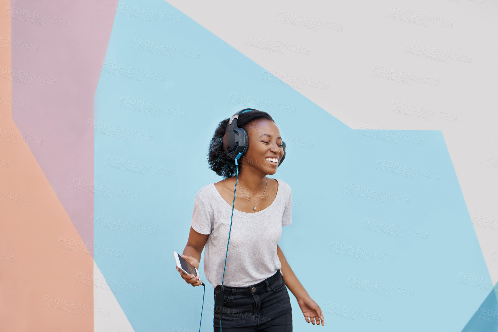 Buy stock photo Shot of a cheerful young woman dancing outside and listening to music on her phone with her eyes closed