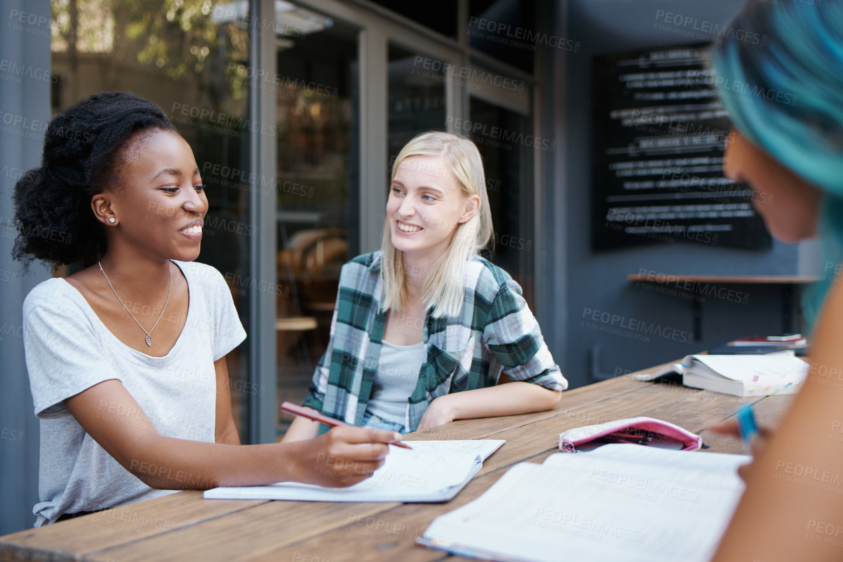 Buy stock photo Students, group and talking outdoor at university with books, writing or learning for education on campus. Friends, gen z people and funny conversation with smile, diversity or college break by table