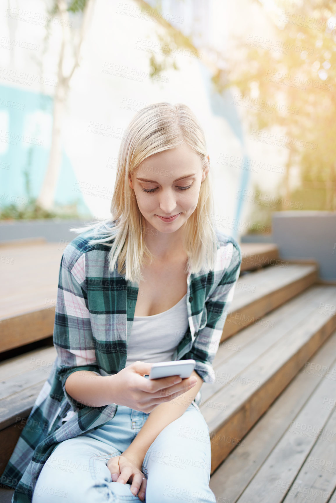 Buy stock photo Shot of a young woman sitting on the steps outside and using a mobile phone