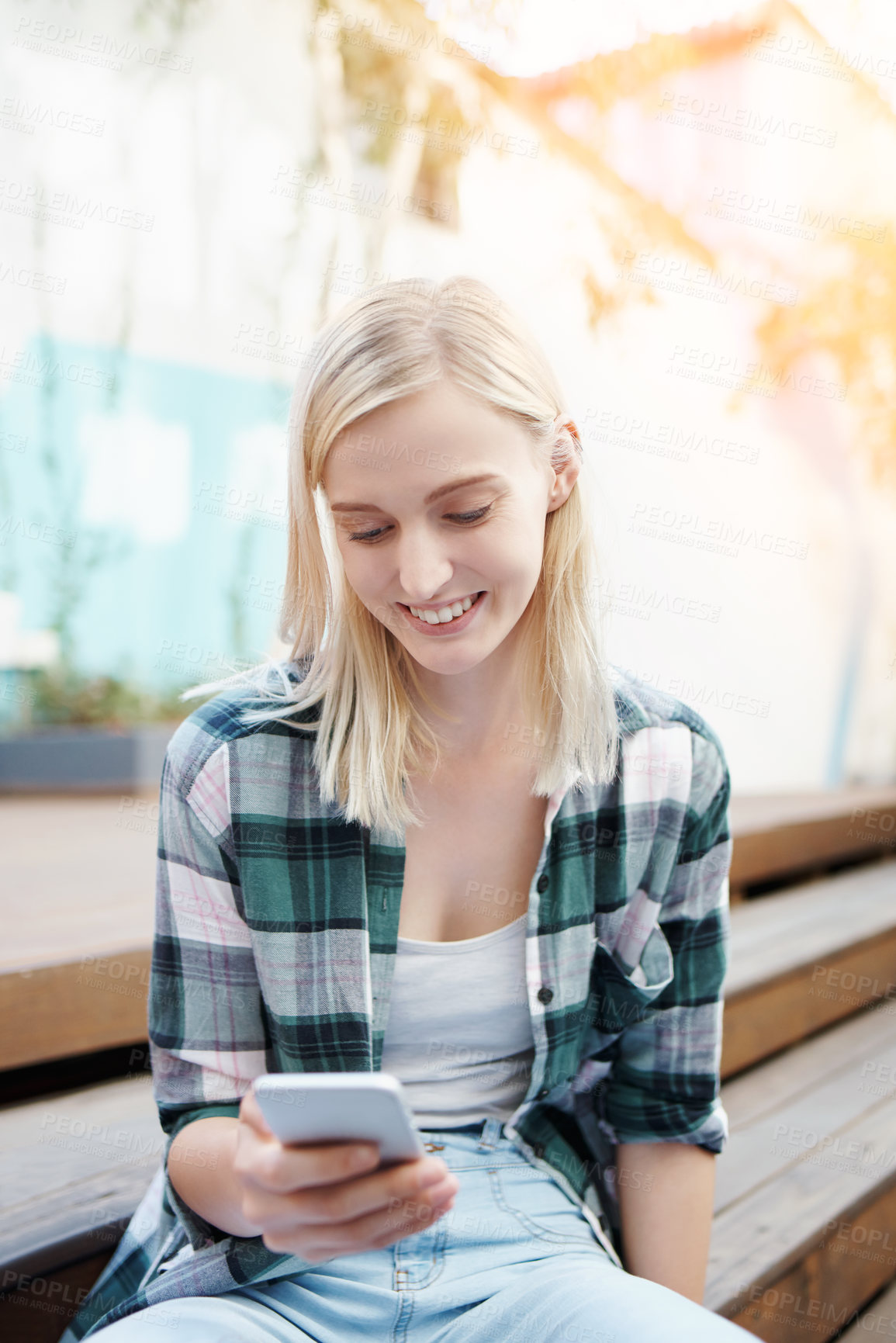 Buy stock photo Shot of a young woman sitting on the steps outside and using a mobile phone