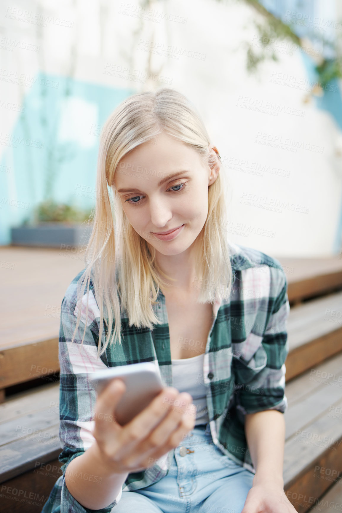 Buy stock photo Shot of a young woman sitting on the steps outside and using a mobile phone