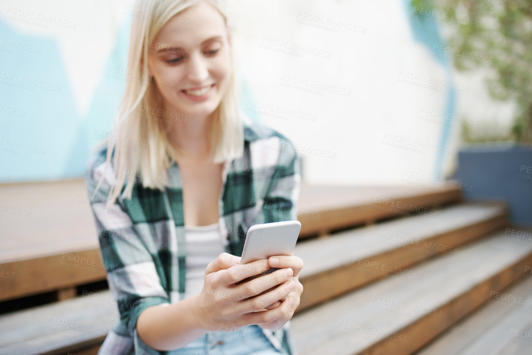 Buy stock photo Shot of a young woman sitting on the steps outside and using a mobile phone