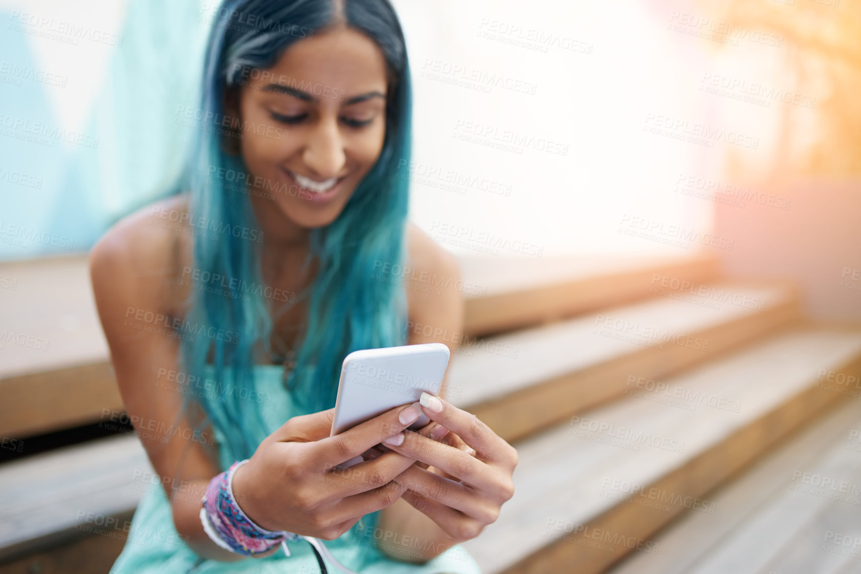 Buy stock photo Shot of a young woman sitting on the steps outside and using a mobile phone